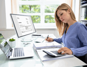 Femme utilisant un ordinateur, une calculatrice et un classeur pour tenir sa comptabilité sans expert-comptable.